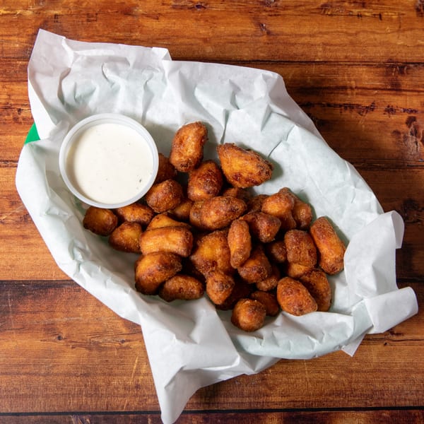 A basket of golden-brown fried cheese curds with a side of ranch dressing on a wooden table.