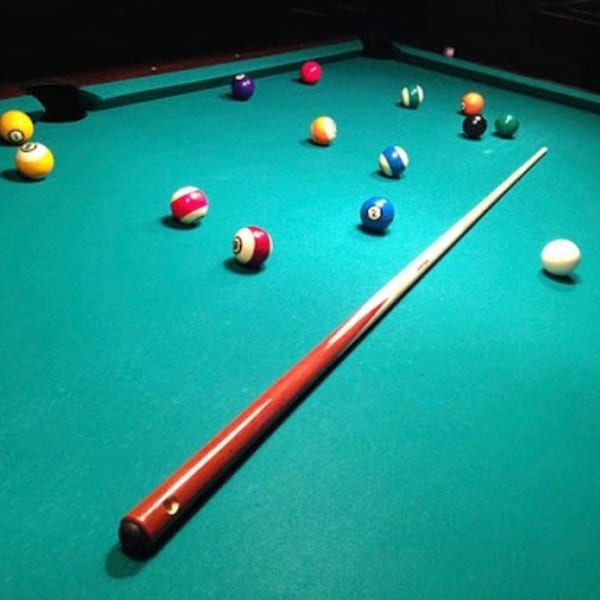 A pool table with scattered billiard balls and a cue stick, ready for a game at Swanky's.