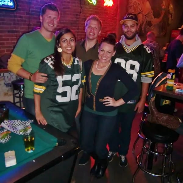 Five friends in Green Bay Packers jerseys and casual attire pose by a pool table at Swanky's.