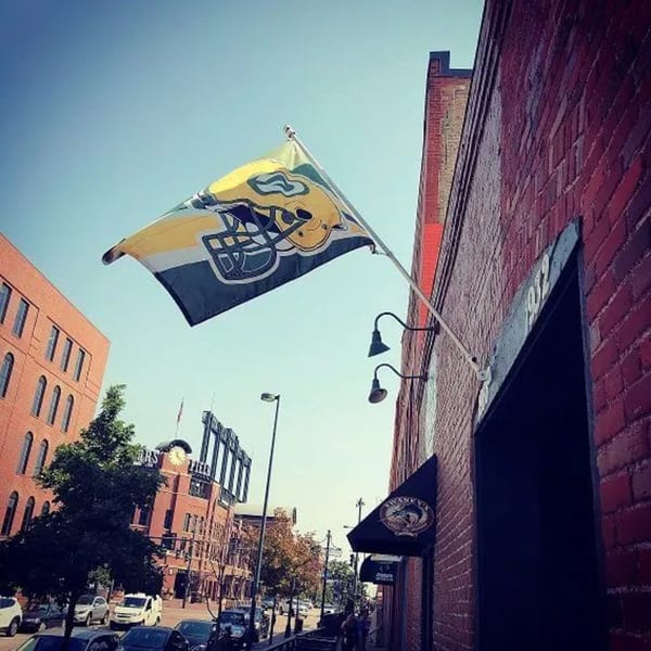 A Swanky's Vittles and Libations flag with a football helmet logo flies outside a brick building.