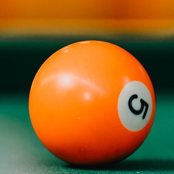Close-up of an orange billiard ball with the number 5 on a green pool table.