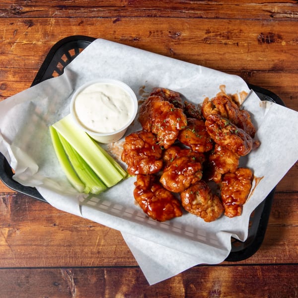Swanky's boneless wings with BBQ sauce, celery sticks, and ranch dressing in a basket.